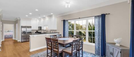 A modern kitchen with white cabinets, a central island, and a dining area with a round table and chairs.