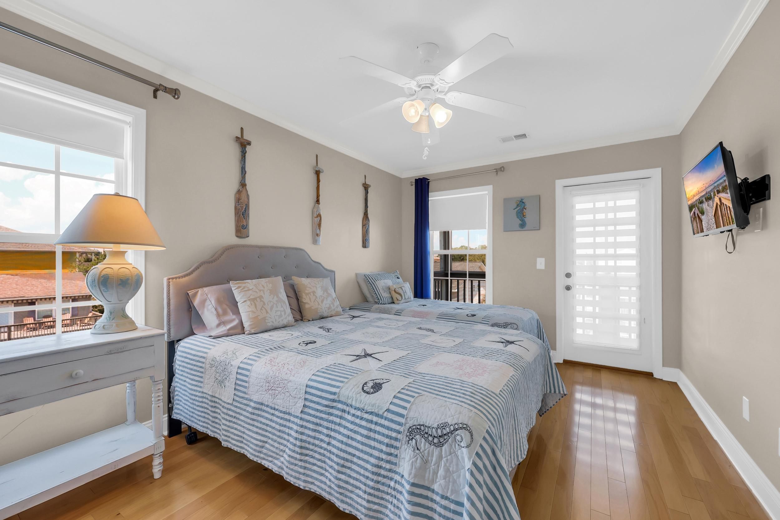 A bedroom with a bed, a nightstand, a lamp, a ceiling fan, and a view of the outdoors through a window.