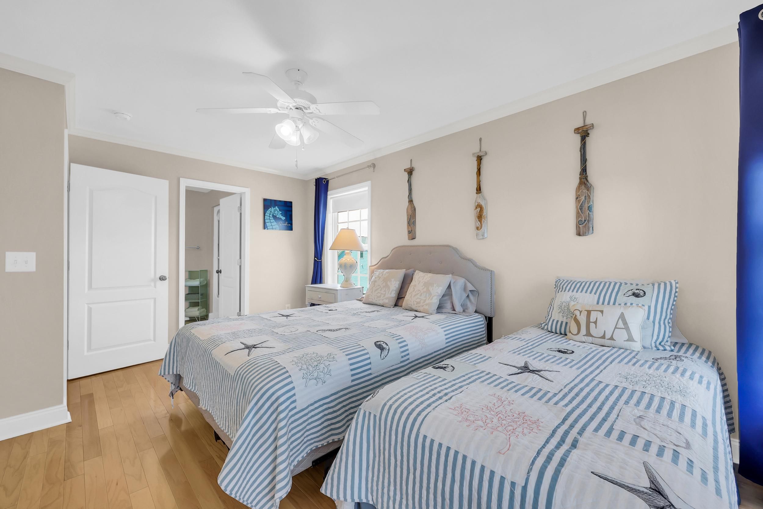A bedroom with two beds, a ceiling fan, and nautical-themed decor.
