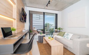 A modern living space with a laptop on a desk, a sofa, a coffee table, and a balcony with a view. - Corporate Stays First del Sol - 208 (Asunción)