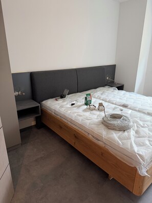 Una camera da letto con una struttura letto in legno, una testiera grigia, un comodino e una piccola mensola.