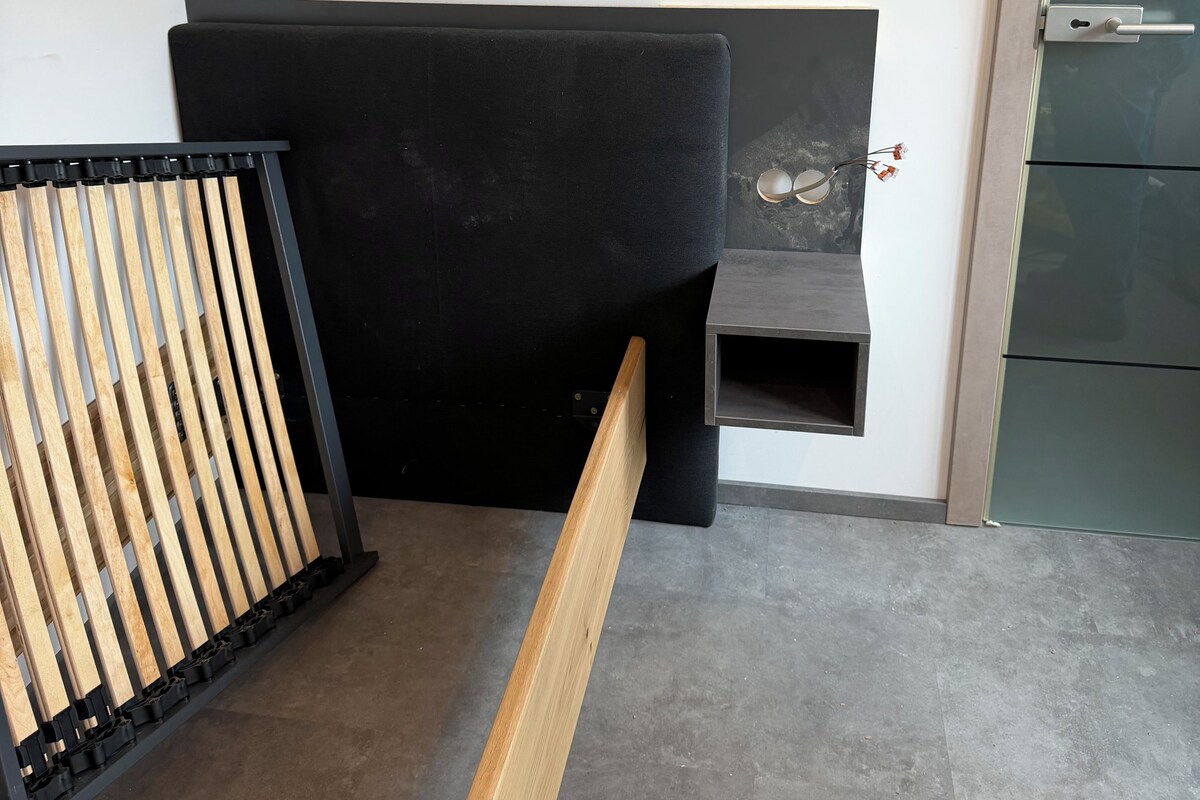 Un angolo di una stanza con una testiera nera imbottita, una panca in legno e una porta verde.