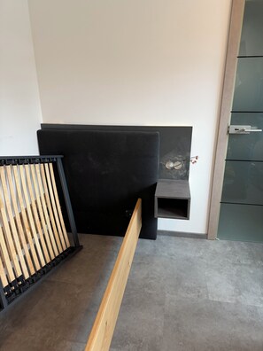 Un angolo di una stanza con una testiera nera imbottita, una panca in legno e una porta verde.