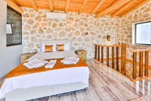 A bedroom with a stone wall, wooden ceiling beams, a bed with white bedding, a nightstand, and a wooden railing. - Serene 1-bedroom Villa With Private Pool in Gelemiş (Kaş)