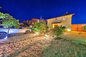 A stone house with a car parked in the driveway, surrounded by a well-lit garden at night. - Serene 1-bedroom Villa With Private Pool in Gelemiş (Kaş)