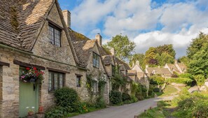 A narrow stone pathway flanked by traditional stone houses with steeply pitched roofs, a green door, and flower boxes. - The Snug at Arlington Mill - Couple's Escape Bibury, Cotswolds (Bibury)