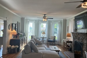 A living room with a sofa, a fireplace, and a ceiling fan. - Large 5-bedroom house in tranquil Cambridge with AC, porches, patio, fire pit (Cambridge)