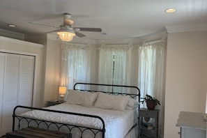A bedroom with a bed, a nightstand, a ceiling fan, and a window with curtains. - Large 5-bedroom house in tranquil Cambridge with AC, porches, patio, fire pit (Cambridge)