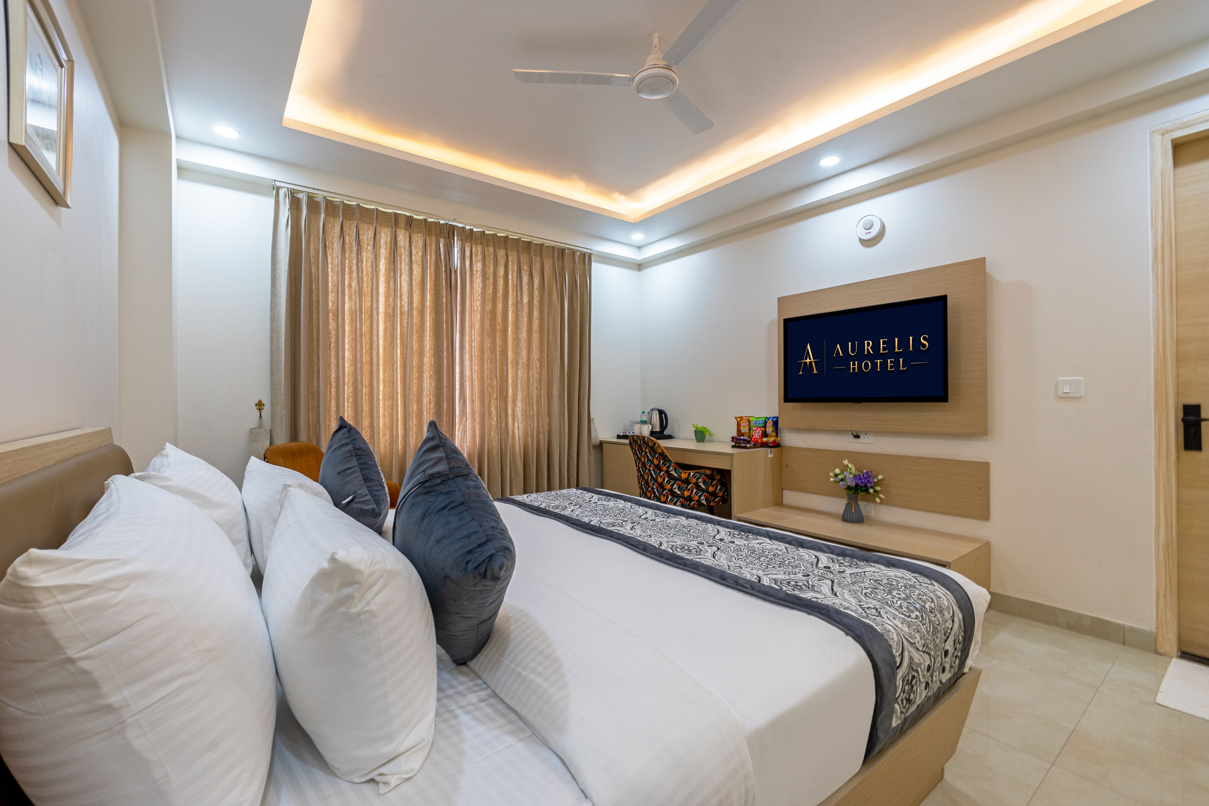 A hotel room with a bed, a desk, a television, and a ceiling fan.