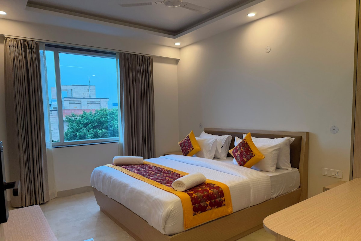 Ein Hotelzimmer mit einem großen Bett, einem Schreibtisch und Blick ins Freie durch ein Fenster.