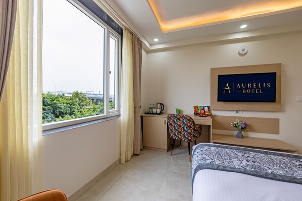 A hotel room with a bed, a desk, a chair, a small kitchenette, and a window with curtains.