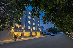 Un hotel de varios pisos con una hilera de tiendas en la planta baja, una calle pavimentada y árboles que enmarcan la escena.