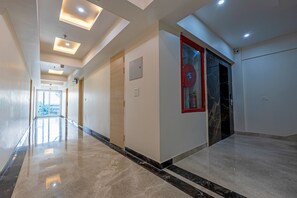 Un pasillo con piso pulido, luces empotradas en el techo y una puerta de marco rojo.