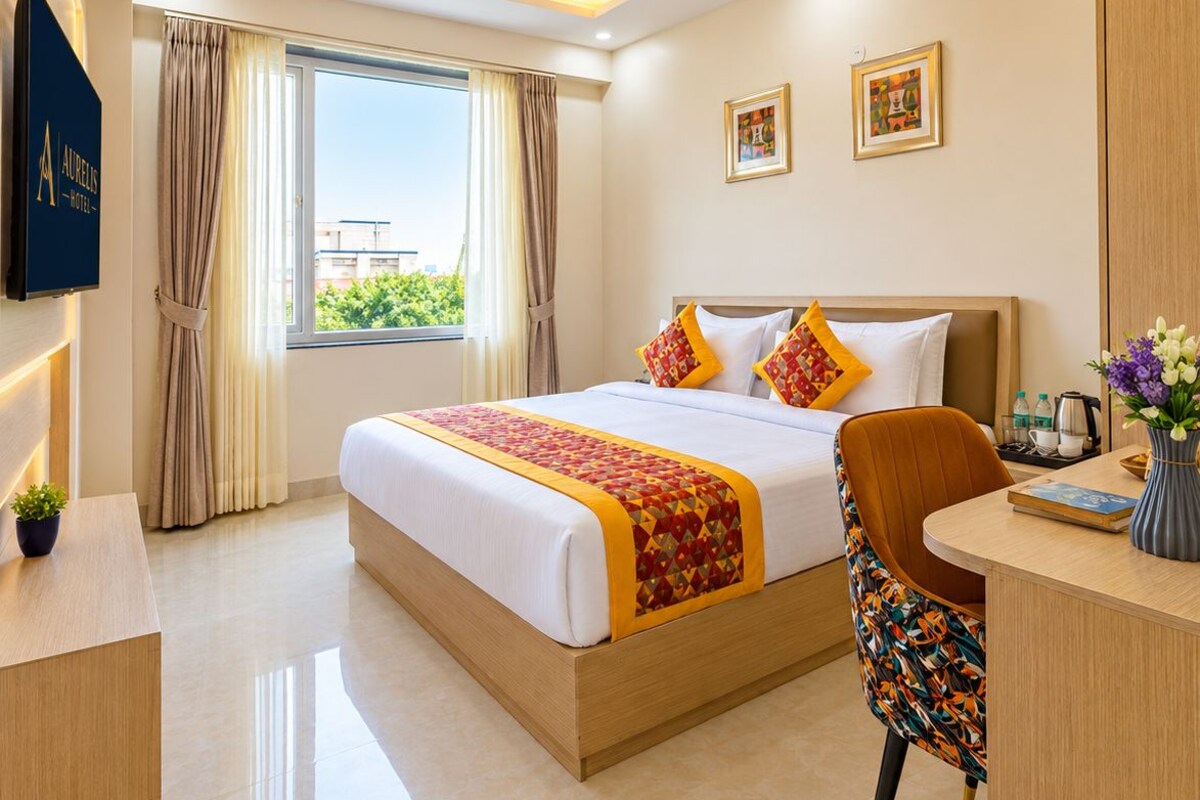 A hotel room with a bed, a desk, a chair, a ceiling fan, and a window with curtains.