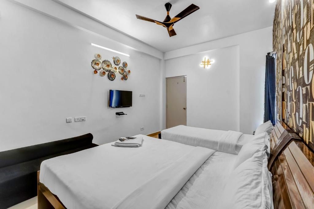 Habitación de hotel con dos camas, un televisor de pantalla plana, ventilador de techo y un adorno en la pared.
