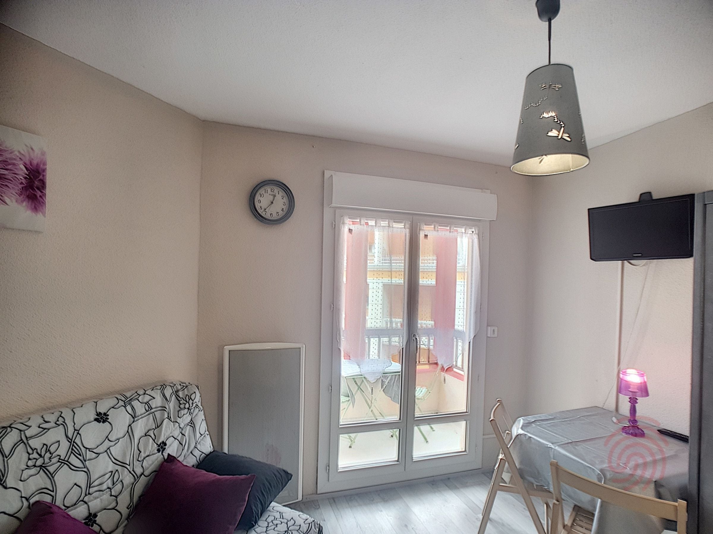 Sala de estar com sofá, mesa, cadeira, relógio e porta de vidro deslizante que dá para área externa.