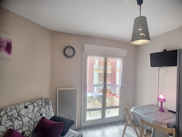 Ein Wohnzimmer mit einer Couch, einem Tisch, einem Sessel, einer Uhr und einer Schiebetür zu einem Außenbereich.