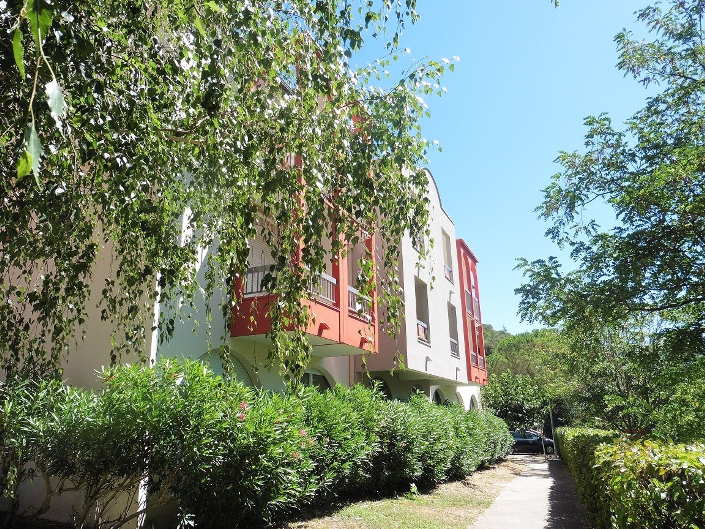 A building with a red and white facade, surrounded by lush greenery and a clear sky.