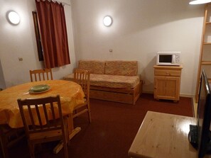 A compact living space with a dining table, chairs, a sofa, a microwave, and a TV. - Spacious studio mountain view - 4 guests (Les Menuires)