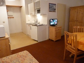 A compact kitchen with white cabinets, a small countertop, and a wooden dining table with chairs. - Spacious studio mountain view - 4 guests (Les Menuires)