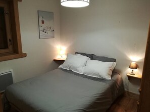 Ein kleines, gemütliches Schlafzimmer mit einem Bett, zwei Nachttischlampen, einem Wandbild und einem Fenster mit Holzrahmen.