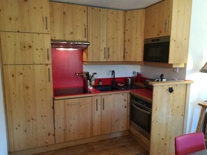 Eine kleine Küche mit Holzschränken, einer roten Arbeitsplatte, einem Edelstahl-Spülbecken und einem eingebauten Backofen.
