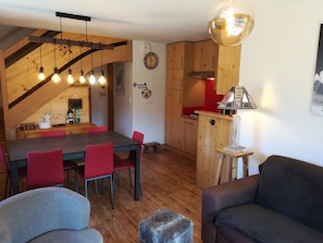 Ein Essbereich mit einem Holztisch und roten Stühlen, eine Küche mit Holzschränken und ein gemütlicher Wohnbereich mit einer Couch und einer Lampe.