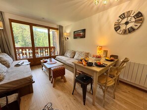 A cozy room with a dining table set for two, a sofa, and a large wall clock. - Cozy apartment, parking - 4 guests (Vars)