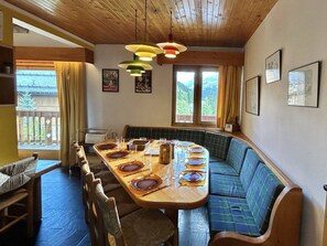 Ein Essbereich mit einem langen Holztisch, gedeckt für sechs Personen, mit blauen, gepolsterten Sitzgelegenheiten an den Seiten.