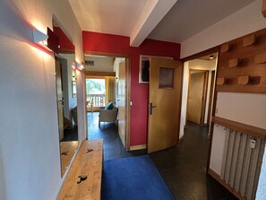 A hallway with a wooden bench, a door leading to a balcony, and a red wall.