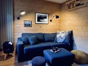 Ein gemütliches Zimmer mit einer Couch, Hocker und einem kleinen Hund.