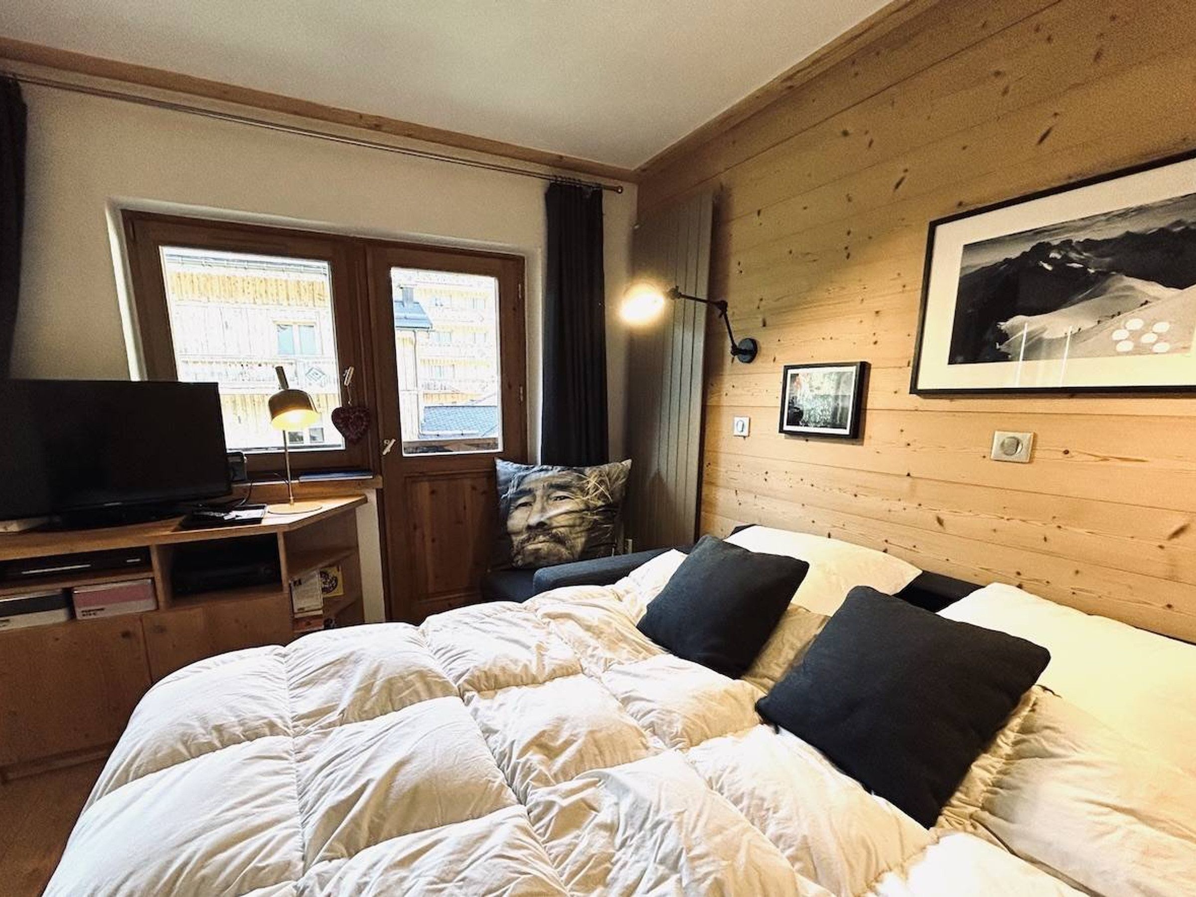 A hotel room with a bed, a desk with a television, and a window with curtains.