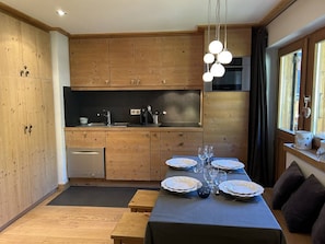 Eine moderne Küche mit Holzschränken, einem eingebauten Ofen und einem Essbereich mit Tisch für vier Personen.