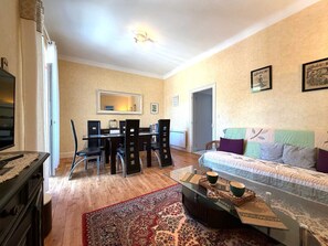 A living room with a sofa, a coffee table, a dining table with chairs, a mirror, and a door. - T3 Apartment mountain view - 5 guests (La Bourboule)