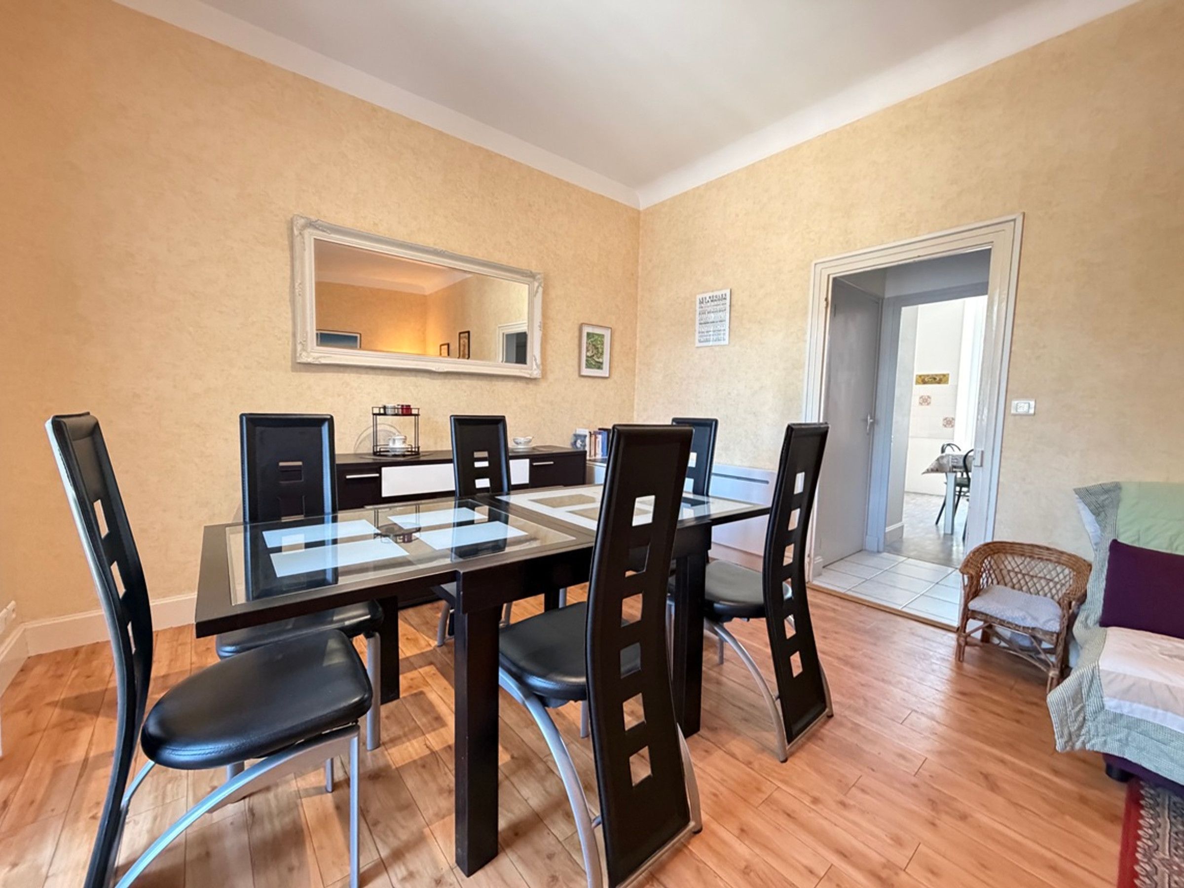 A dining area with a glass-top table, black chairs, and a mirror on the wall.