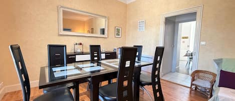 Uma área de refeições com mesa de vidro, cadeiras pretas e espelho na parede.
