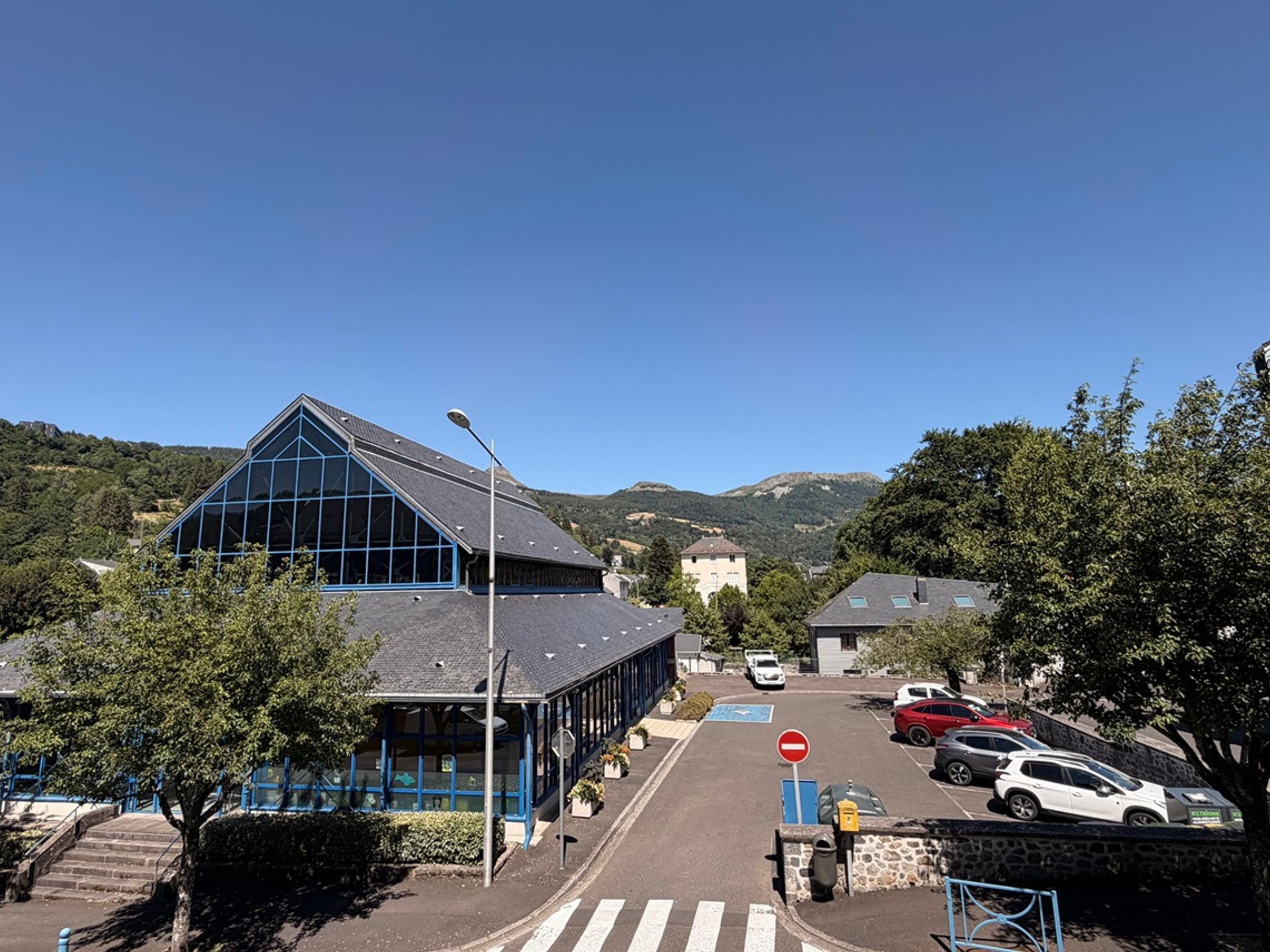 A street view with a modern building, parked cars, and a clear sky.