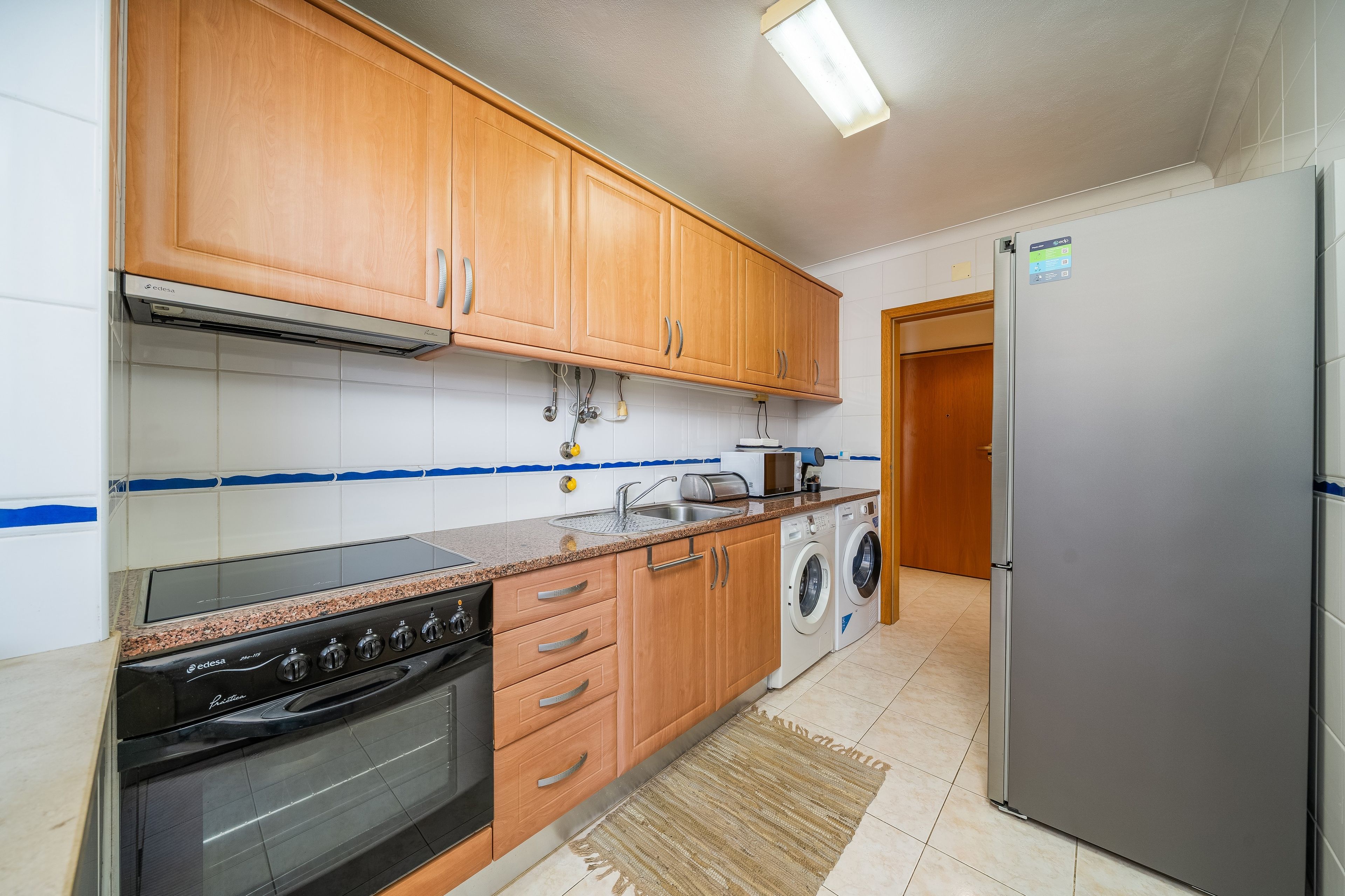 A kitchen with wooden cabinets, a stainless steel refrigerator, a washing machine, and a stove.