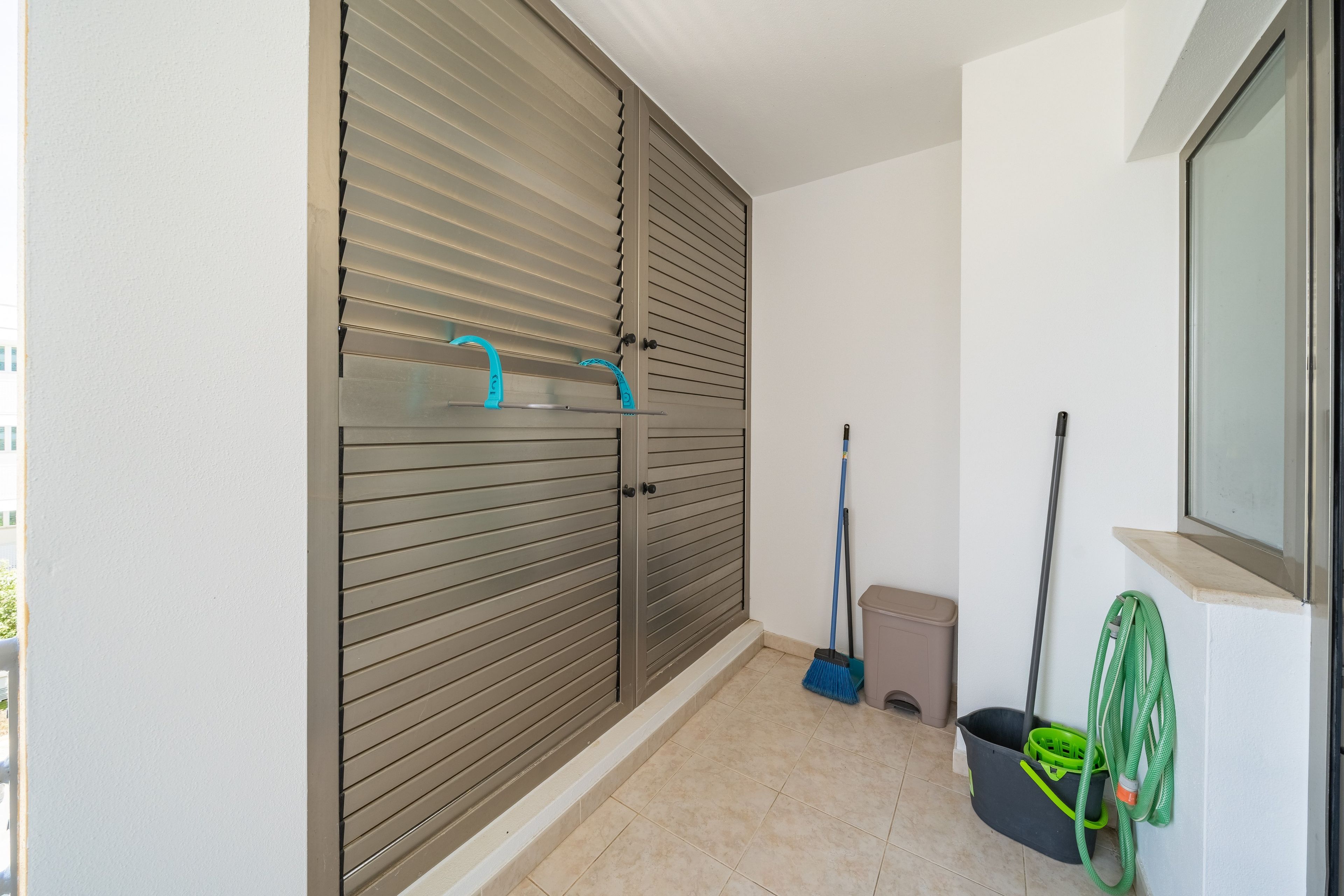 Une pièce avec une porte coulissante, un balai, une pelle et un tuyau d’arrosage vert.