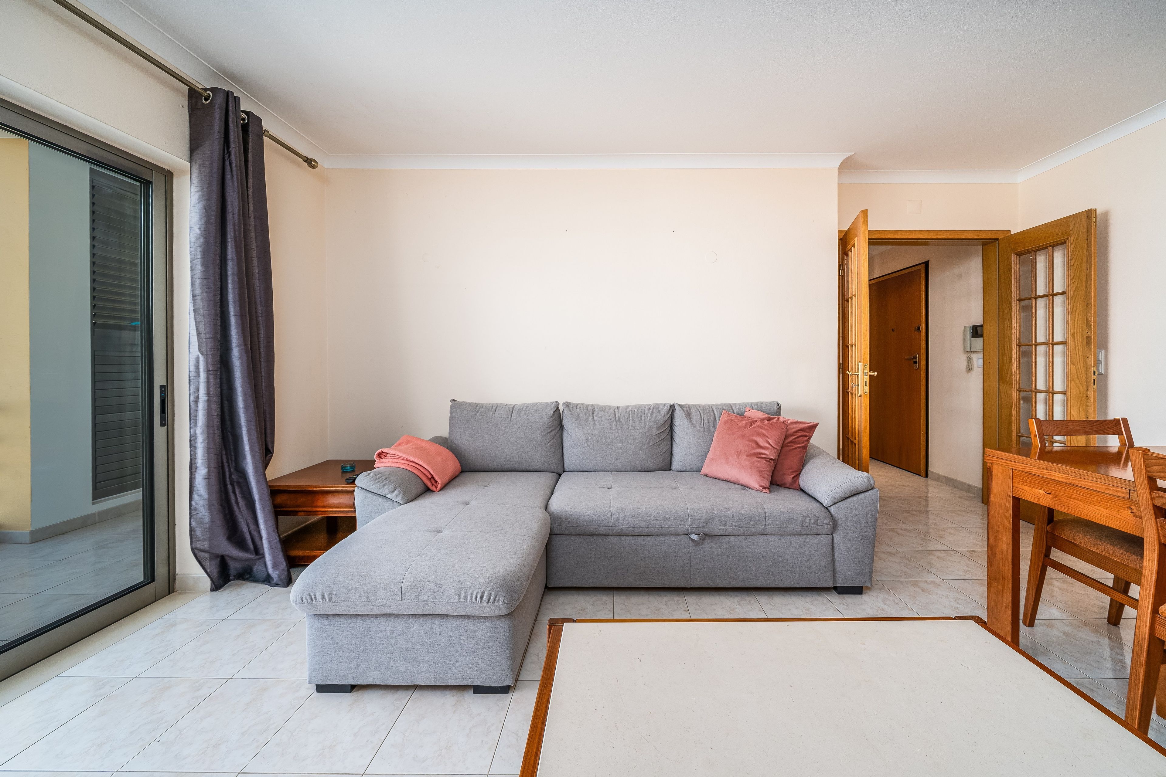 A modern living room with a grey sectional sofa, a wooden dining table, and a sliding glass door.