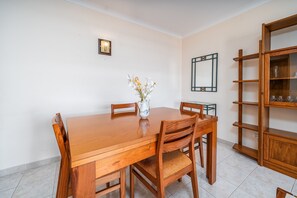 Un coin repas avec une table et des chaises en bois, un vase rempli de fleurs et une bibliothèque.