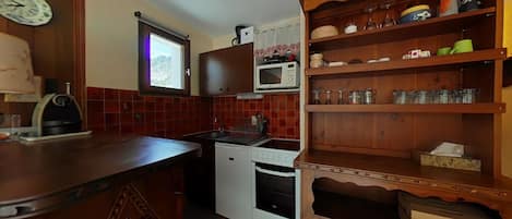 Una cocina compacta con microondas, fregadero y un armario de madera con estantes.