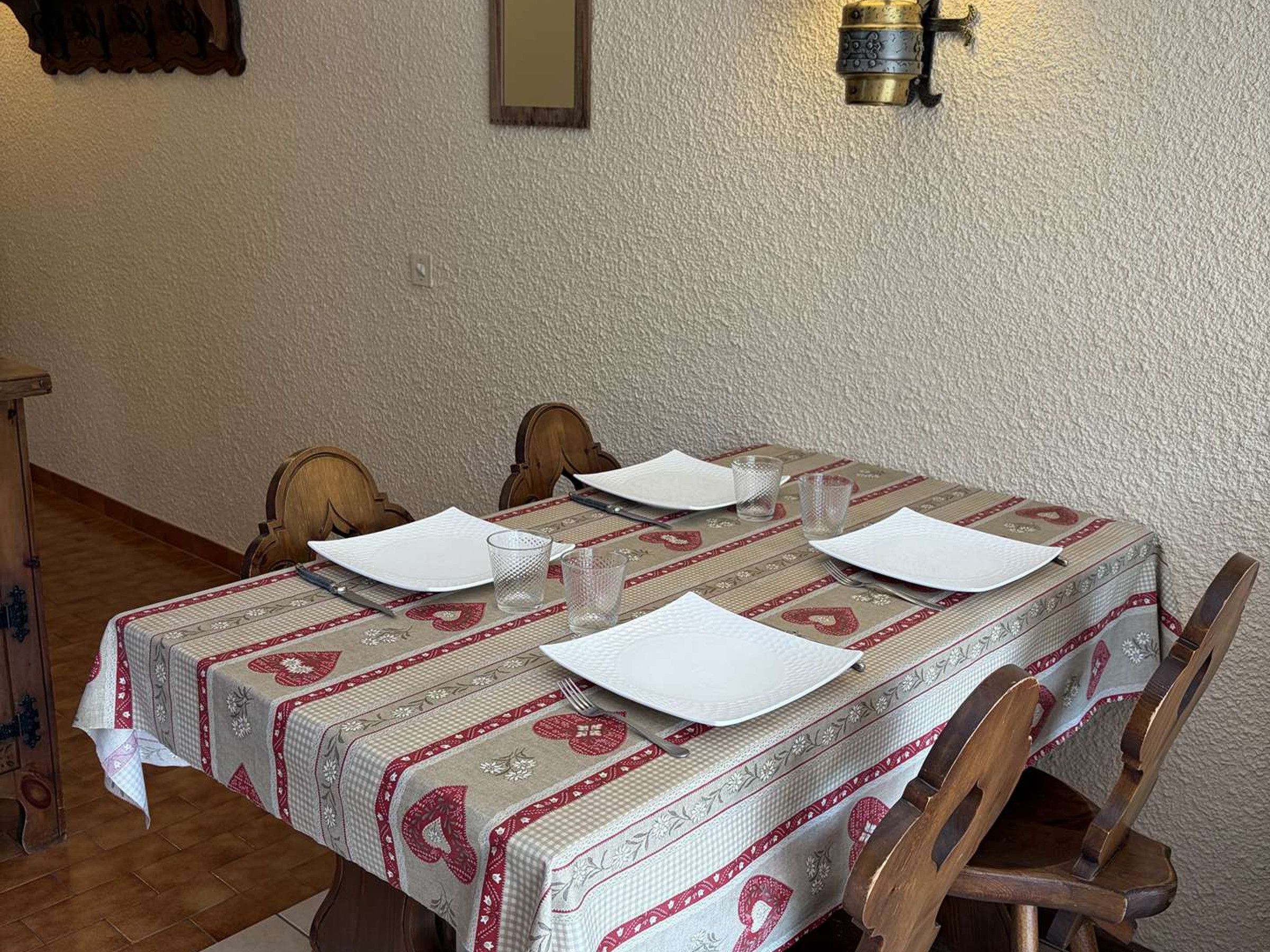 Ein Esstisch ist mit weißen Tellern, Gläsern und Besteck gedeckt, bedeckt mit einer gemusterten Tischdecke.
