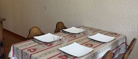 Een eettafel gedekt met witte borden, glazen en bestek, afgedekt met een tafelkleed met een patroon.