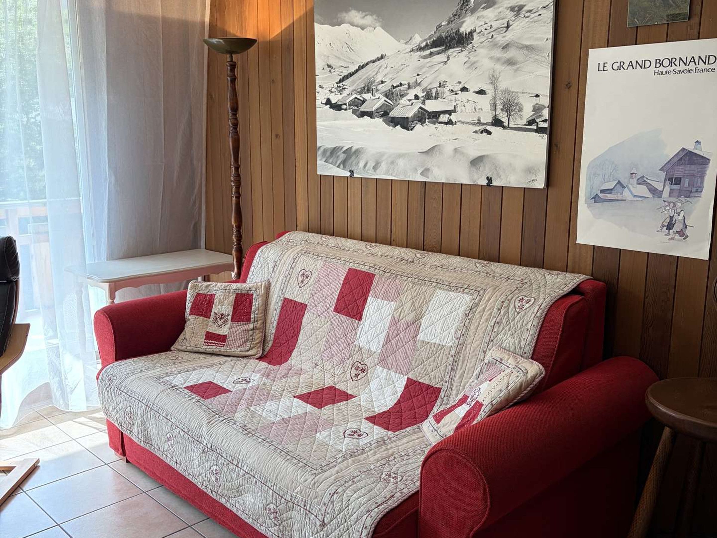 A red sofa with a quilt, a lamp, and two framed pictures on the wall.