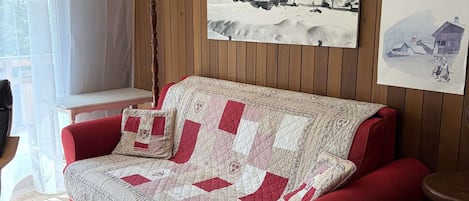 A red sofa with a quilt, a lamp, and two framed pictures on the wall.