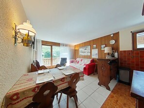A dining area with a table set for four, a red sofa, a wooden cabinet, and a view through a window. - Studio cabin with slope view - 4 guests (Le Grand-Bornand)