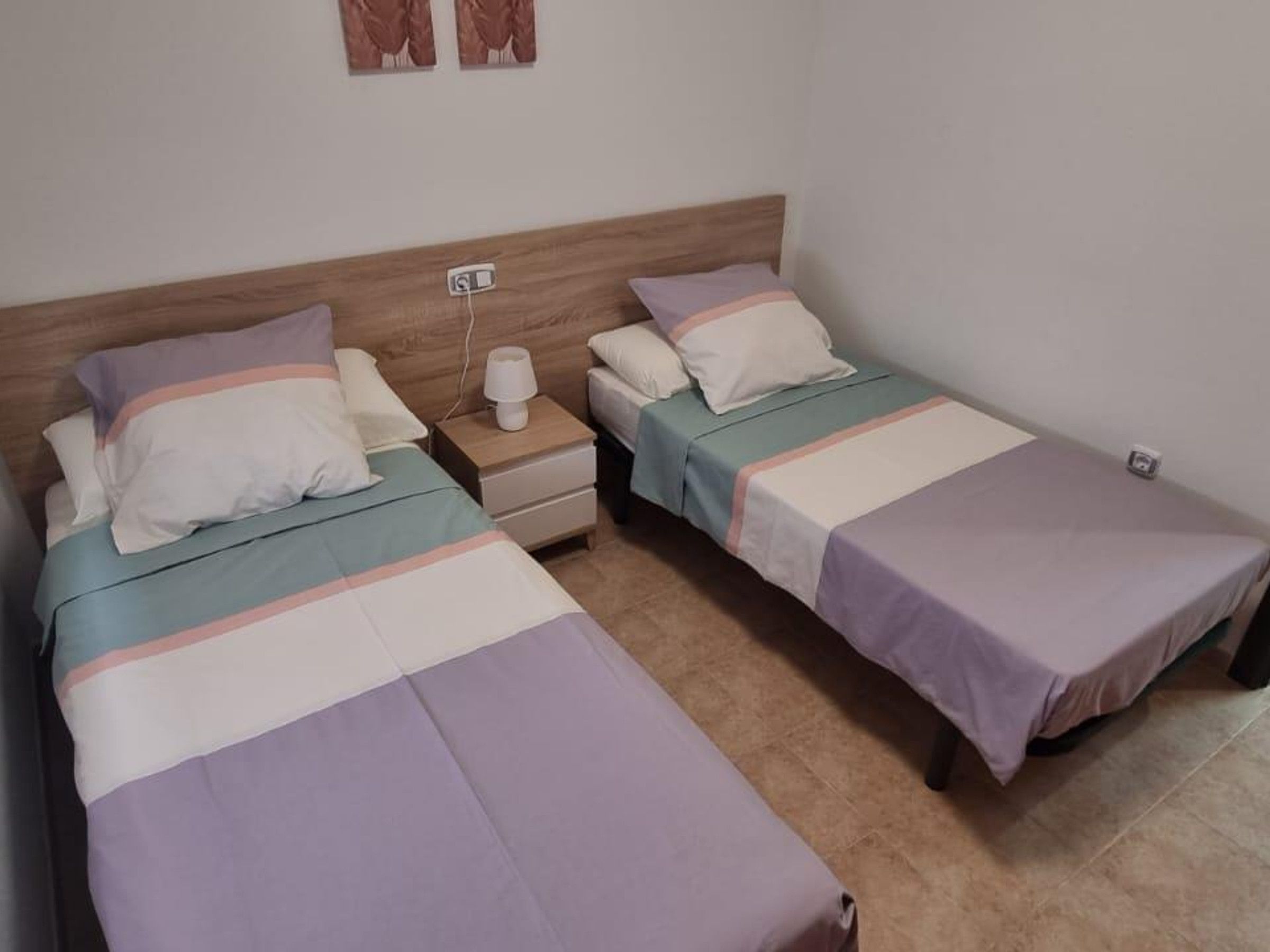 A room with two single beds, each with a nightstand and a lamp.