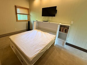 A bedroom with a bed, a TV mounted on the wall, a window with blinds, and a bookshelf. - Updated 3 bedroom condo- walking distance to ski slopes! (Sugar Mountain)