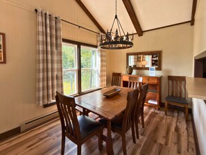 A dining area with a wooden table and chairs, a chandelier, and a view through large windows. - Updated 3 bedroom condo- walking distance to ski slopes! (Sugar Mountain)